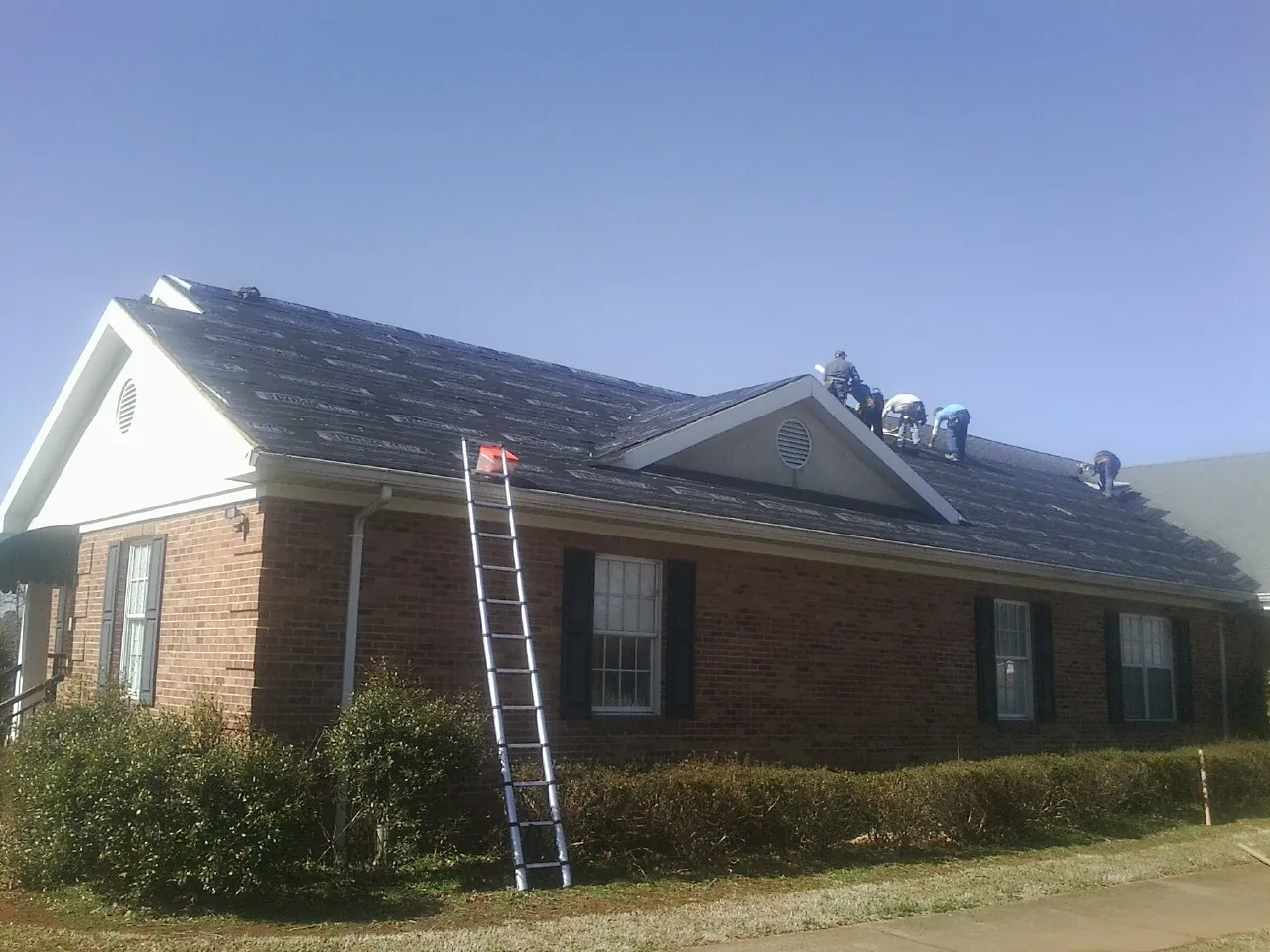 Crew tearing shingles off a brick ranch roof with a ladder set — Emergency Roof Repair work by our crew in Decorah