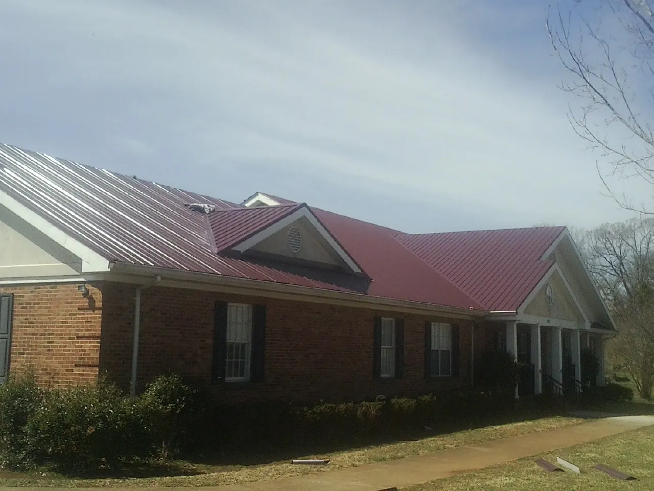 Red metal roof with gabled entries on a long brick building, from a Hail Damage Roof Repair job in Decorah