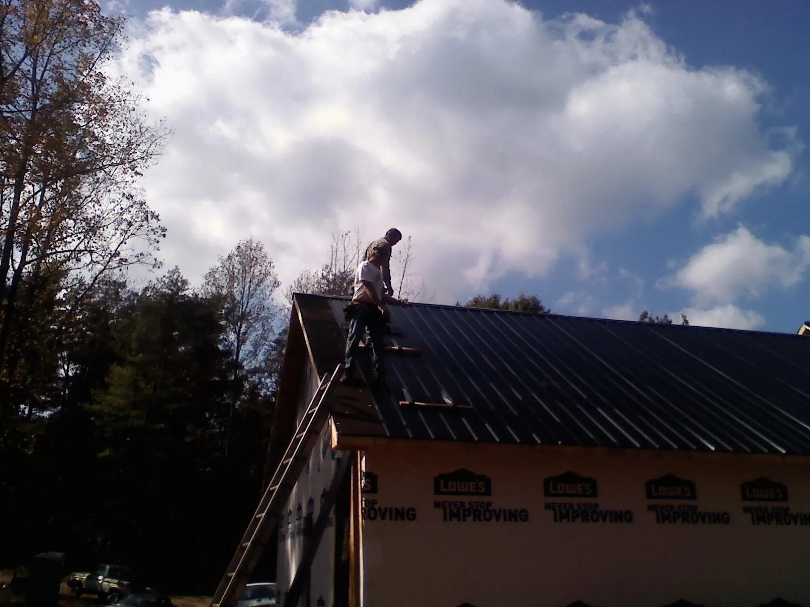 Roofer fastening dark metal panels high against a cloudy sky, from a Roof Inspection job in Decorah
