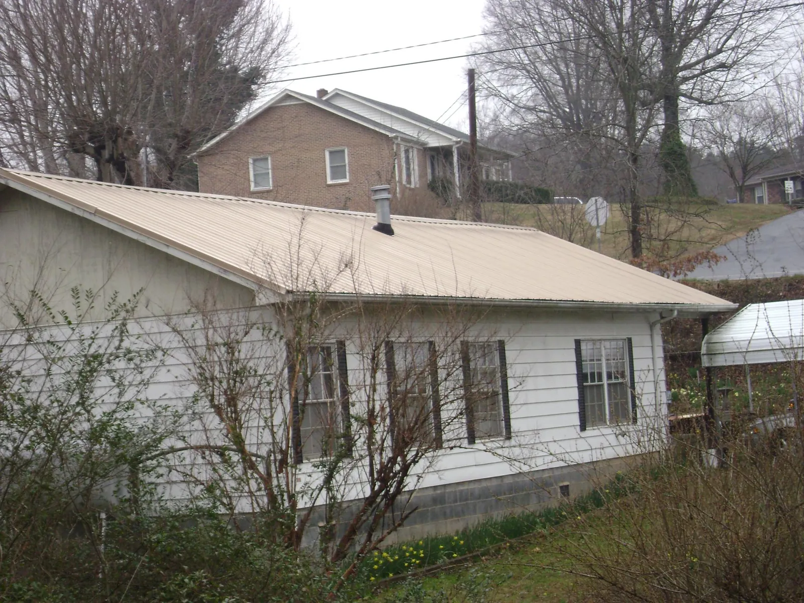 Tan metal roof on a white sided house set into a hillside — Commercial Roofing by Roofing Brothers in Decorah