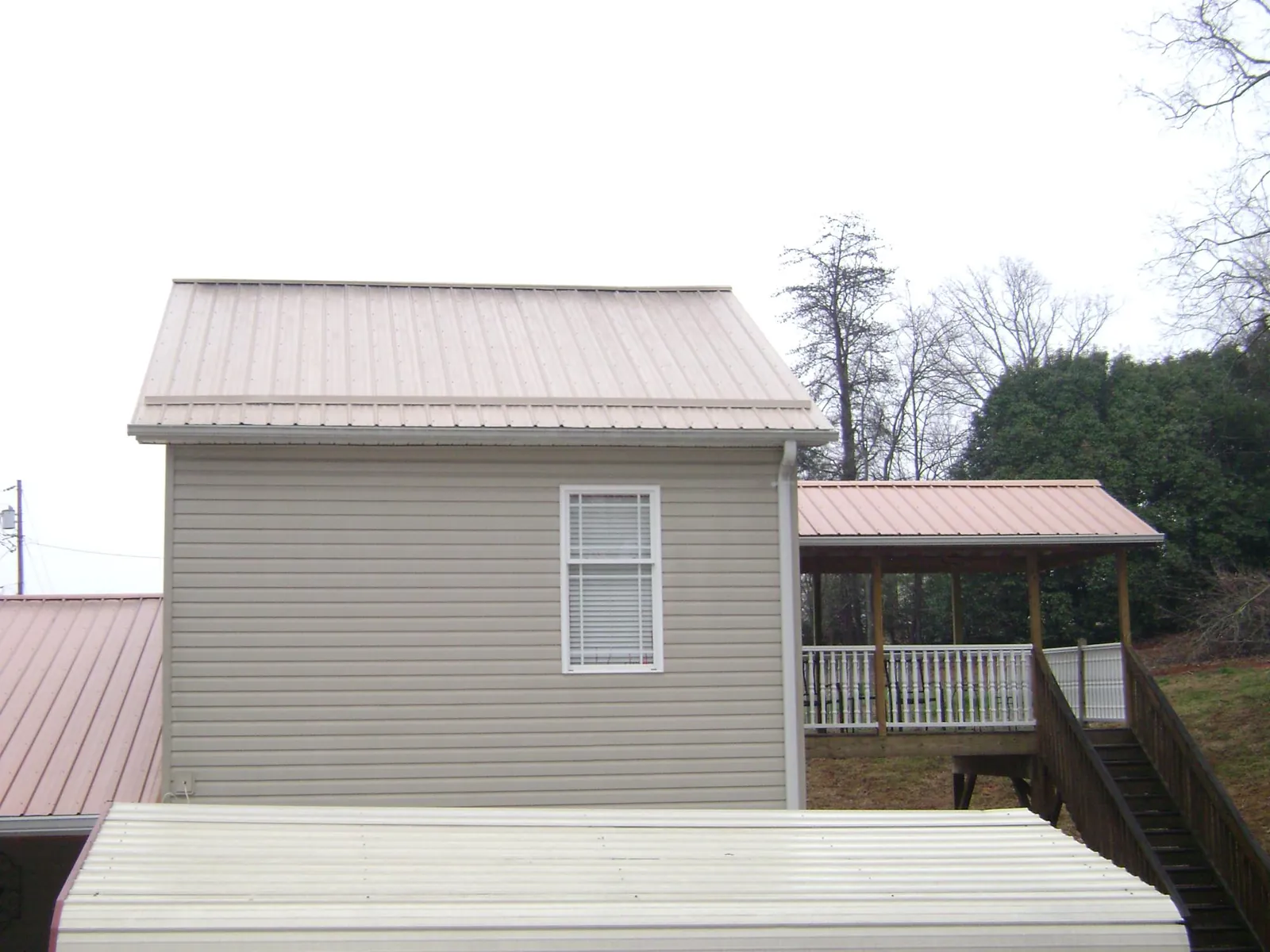 Tan metal roofs on a two story addition and attached porch, from a Roof Replacement job in Decorah