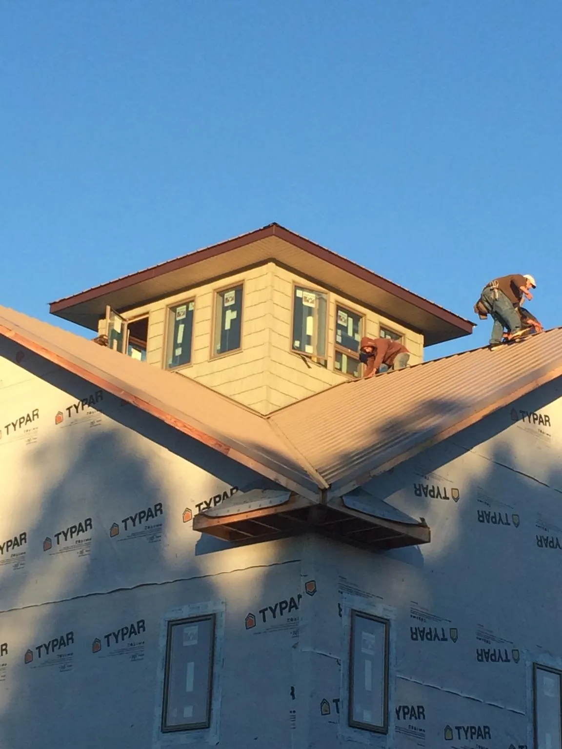 Roofers working around a rooftop cupola on a new metal roof at sunset — Roof Waterproofing in Decorah by Roofing Brothers